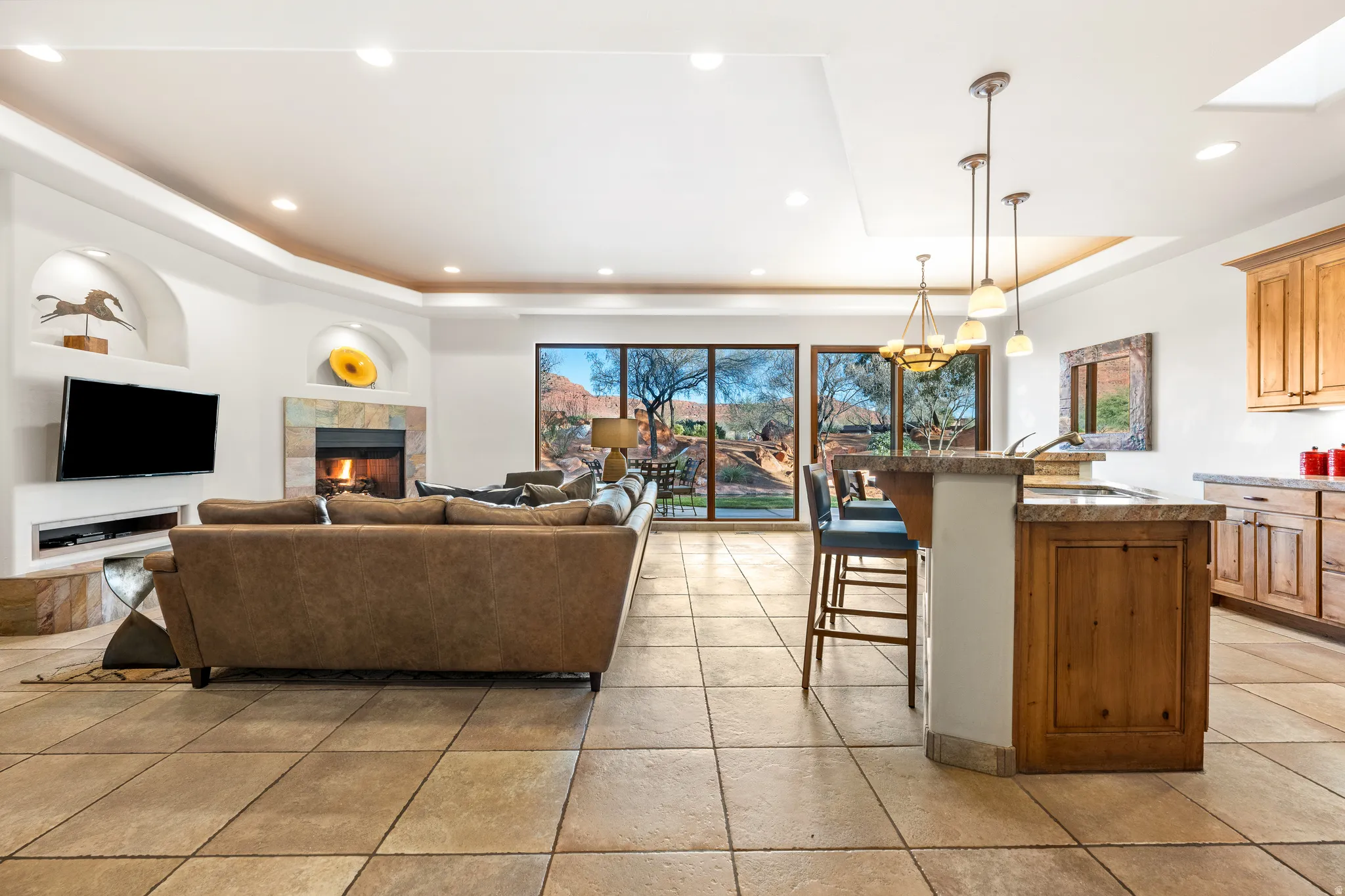 Expansive tile flooring, integrated fireplace with stone surround, recessed lighting, and a kitchen island with pendant lighting