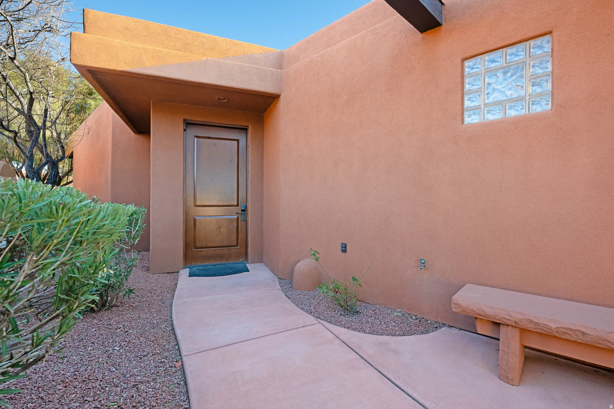 Stucco exterior with a covered entry, wood-paneled door, glass block window, and a concrete pathway with gravel landscaping