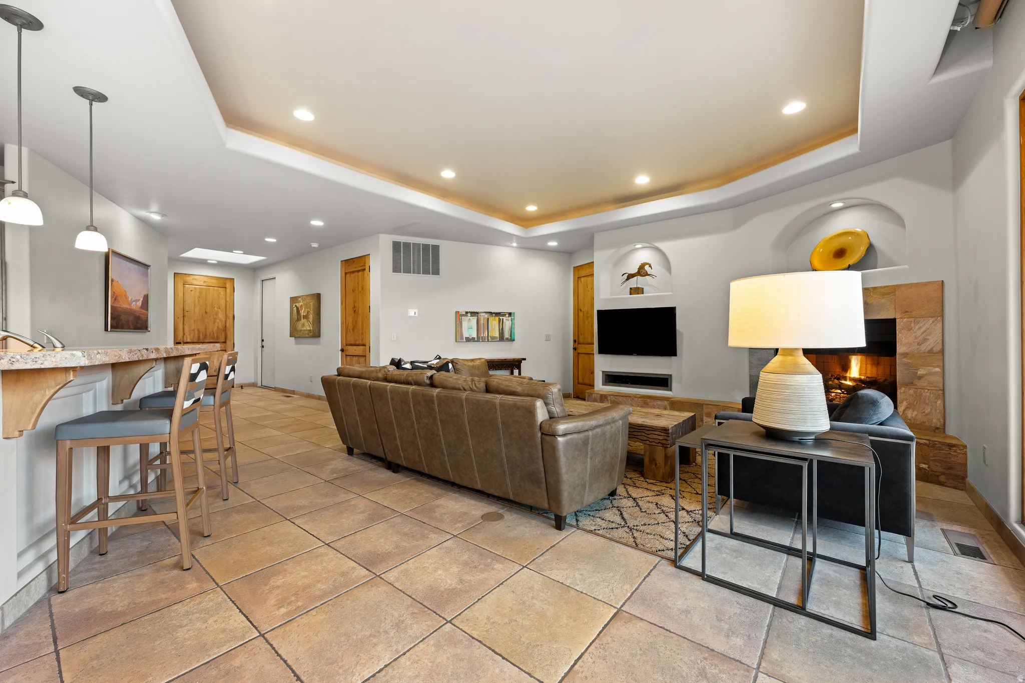 Recessed lighting, tray ceiling, tile flooring, stone-clad fireplace, and built-in shelving