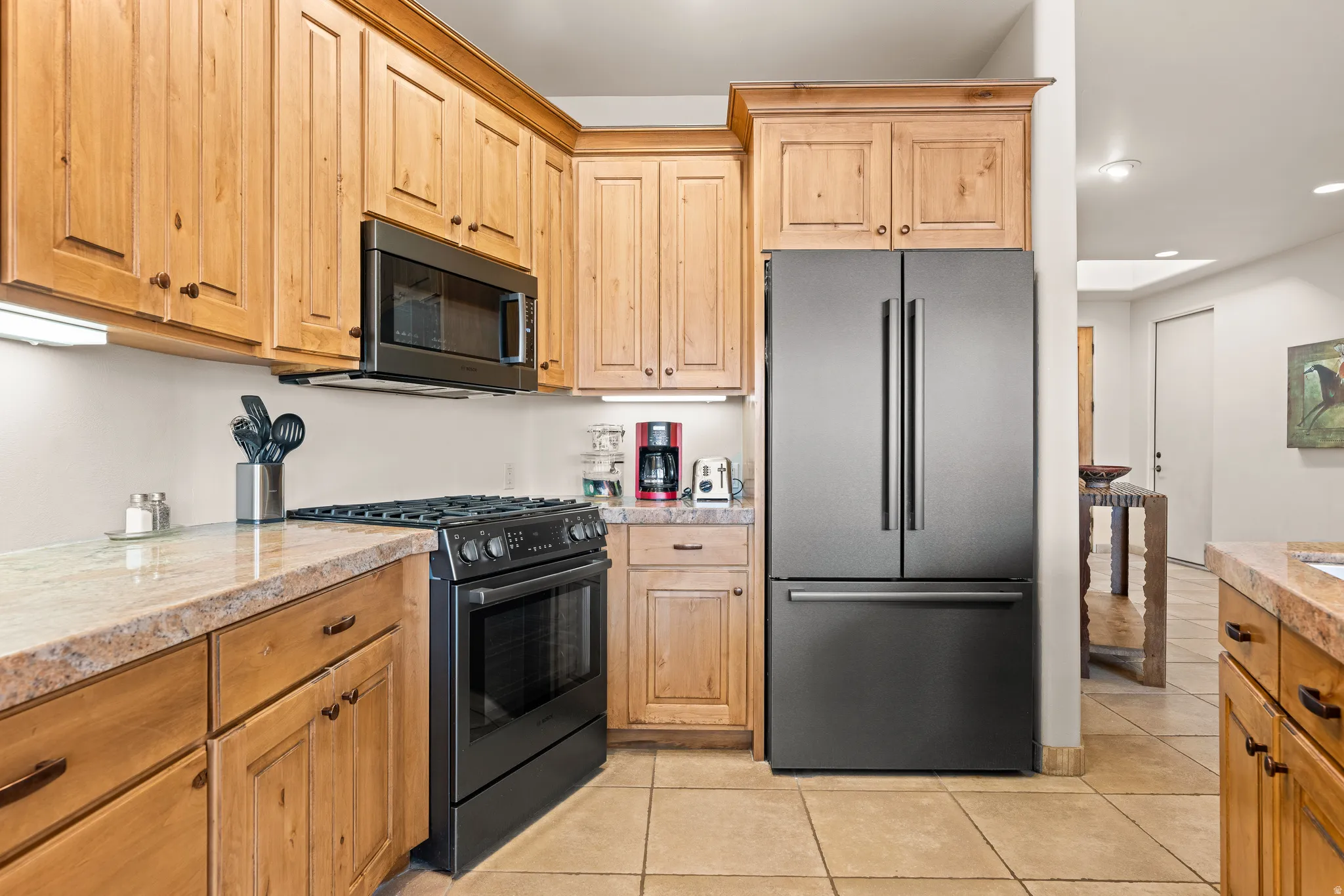 Kitchen featuring light wood cabinetry, stone-finish countertops, and black appliances