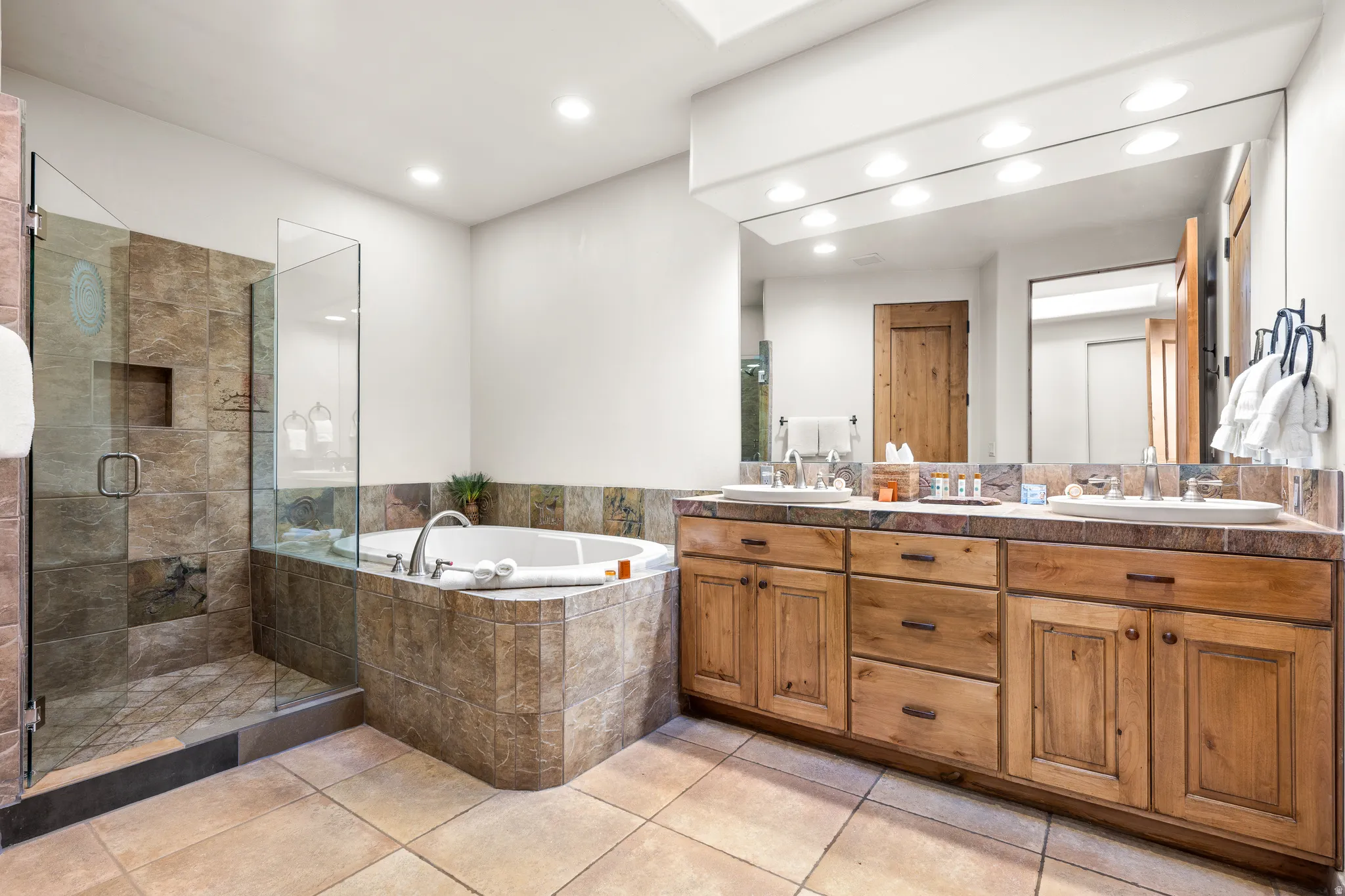 Dual vanity with wood-finish cabinetry, tile countertop, and undermount sinks
