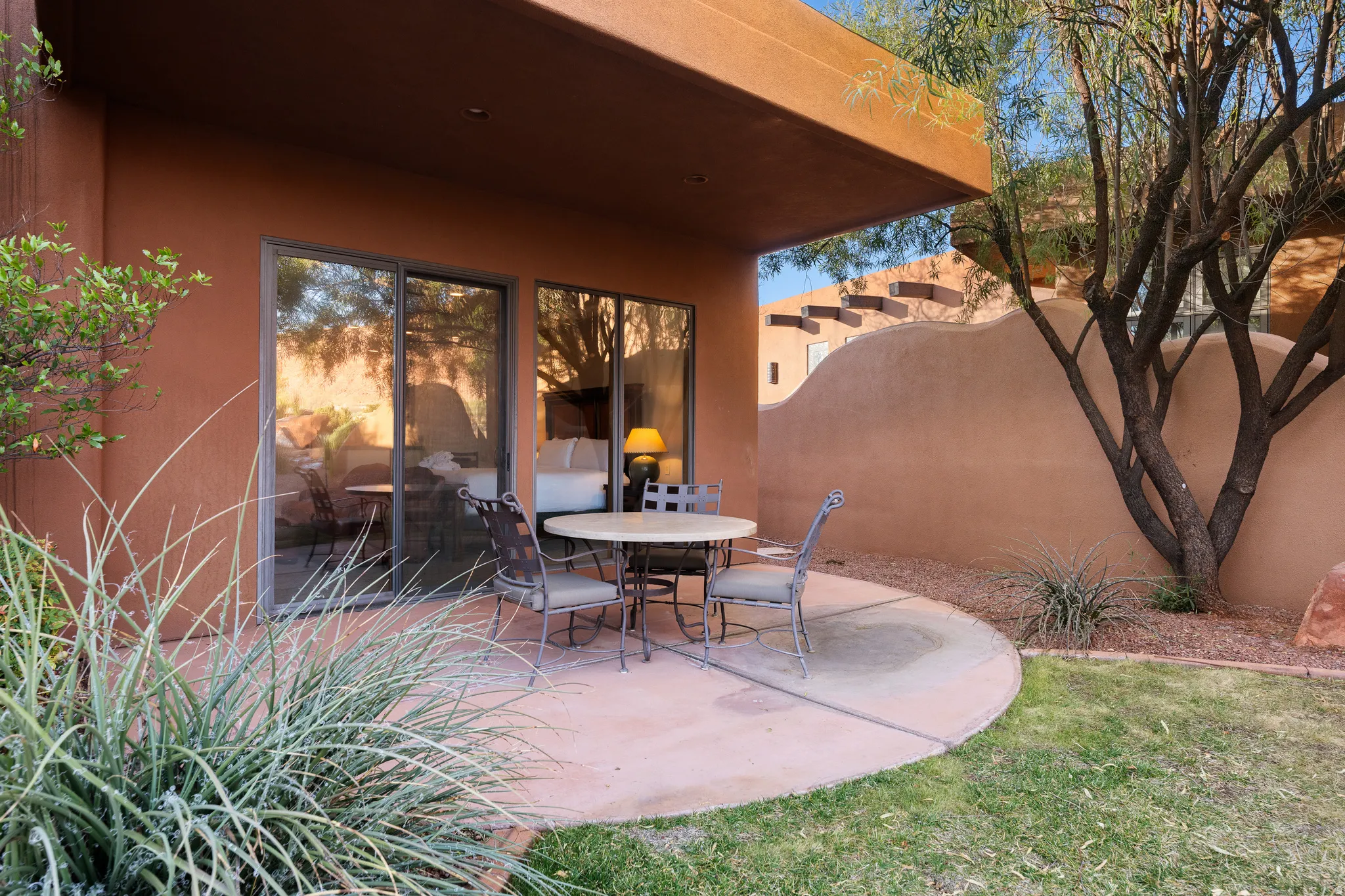 Covered patio with a curved concrete slab, glass sliding doors, and mature desert landscaping