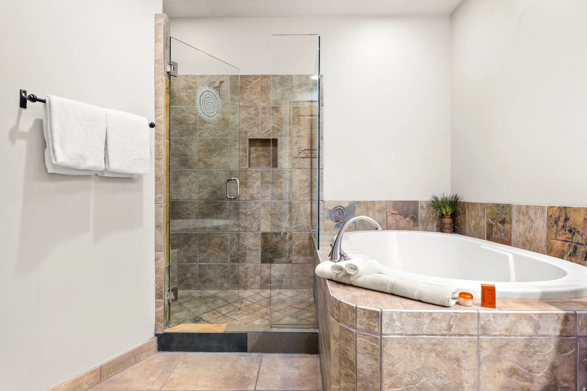 Walk-in shower with glass enclosure and tiled surround, separate soaking tub with tiled deck, and complementary tiled flooring