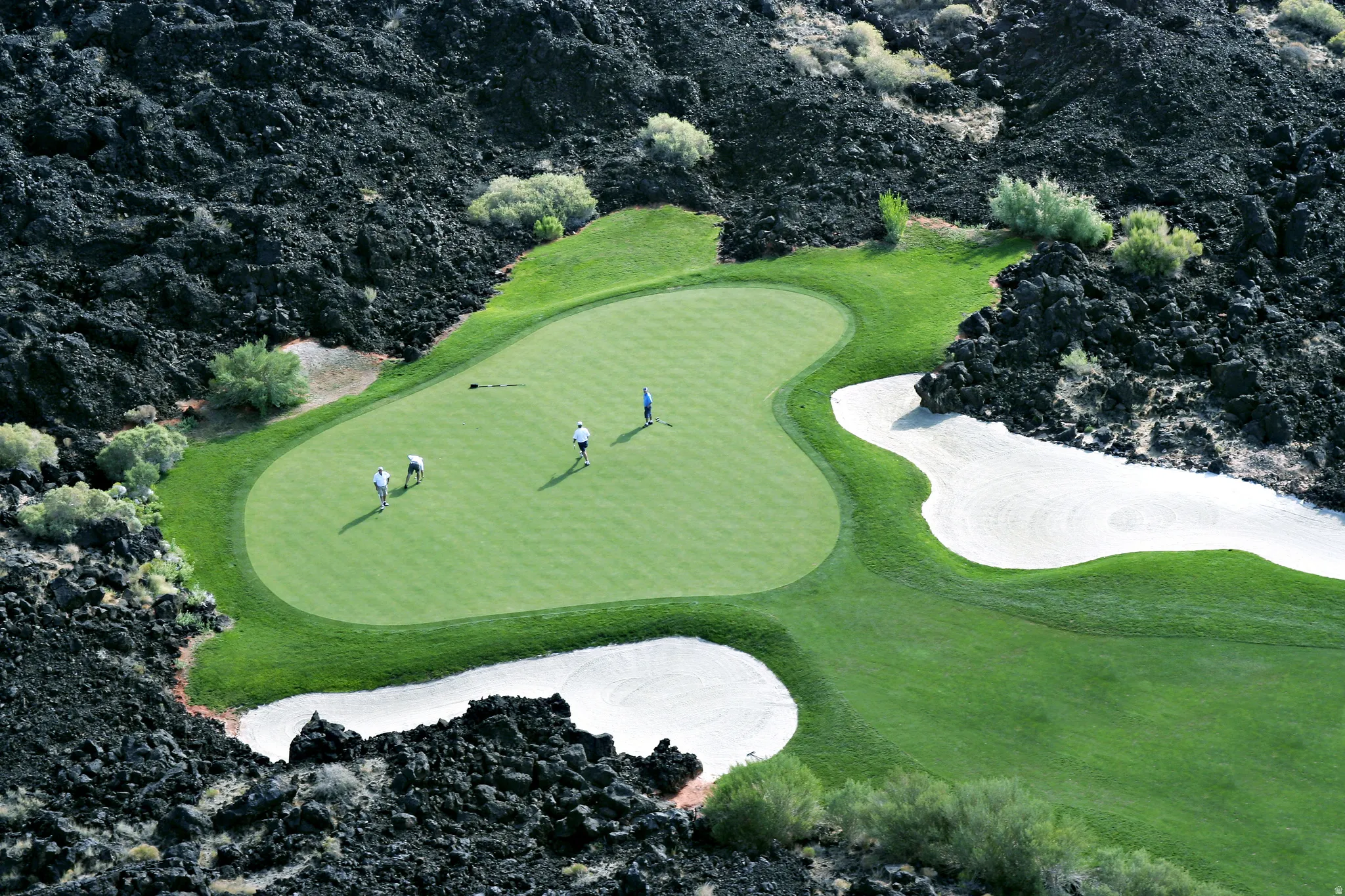 Golf course green surrounded by dark rock formations and sand traps