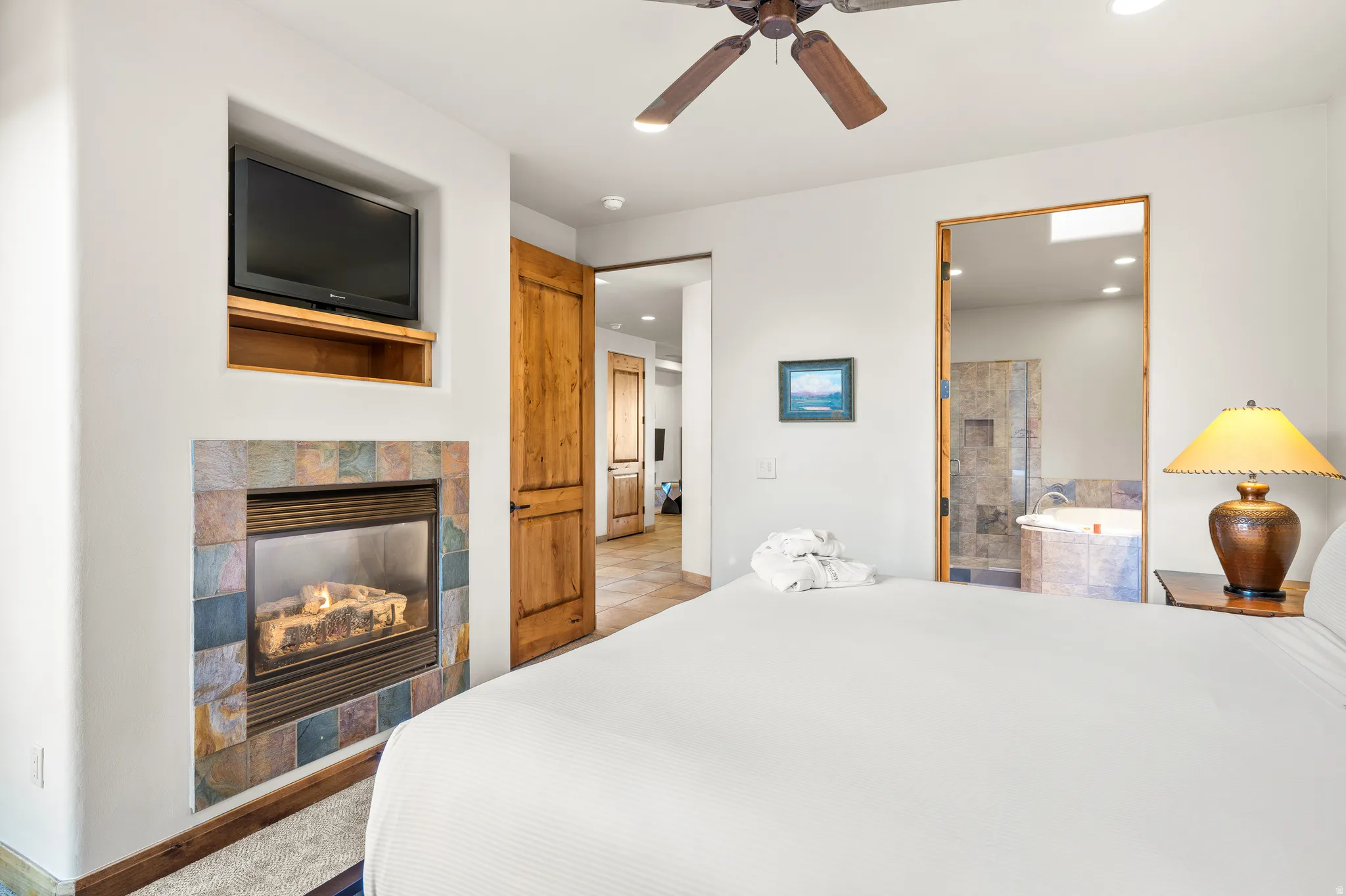 Gas fireplace with a tile surround, built-in media niche, wood-finish ceiling fan, and solid wood door