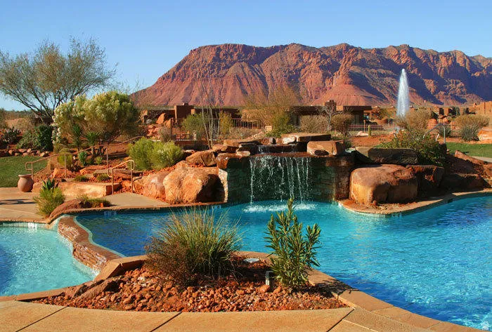 Multi-tiered pool with rock waterfall feature, surrounding desert landscaping, and a distant mountain backdrop