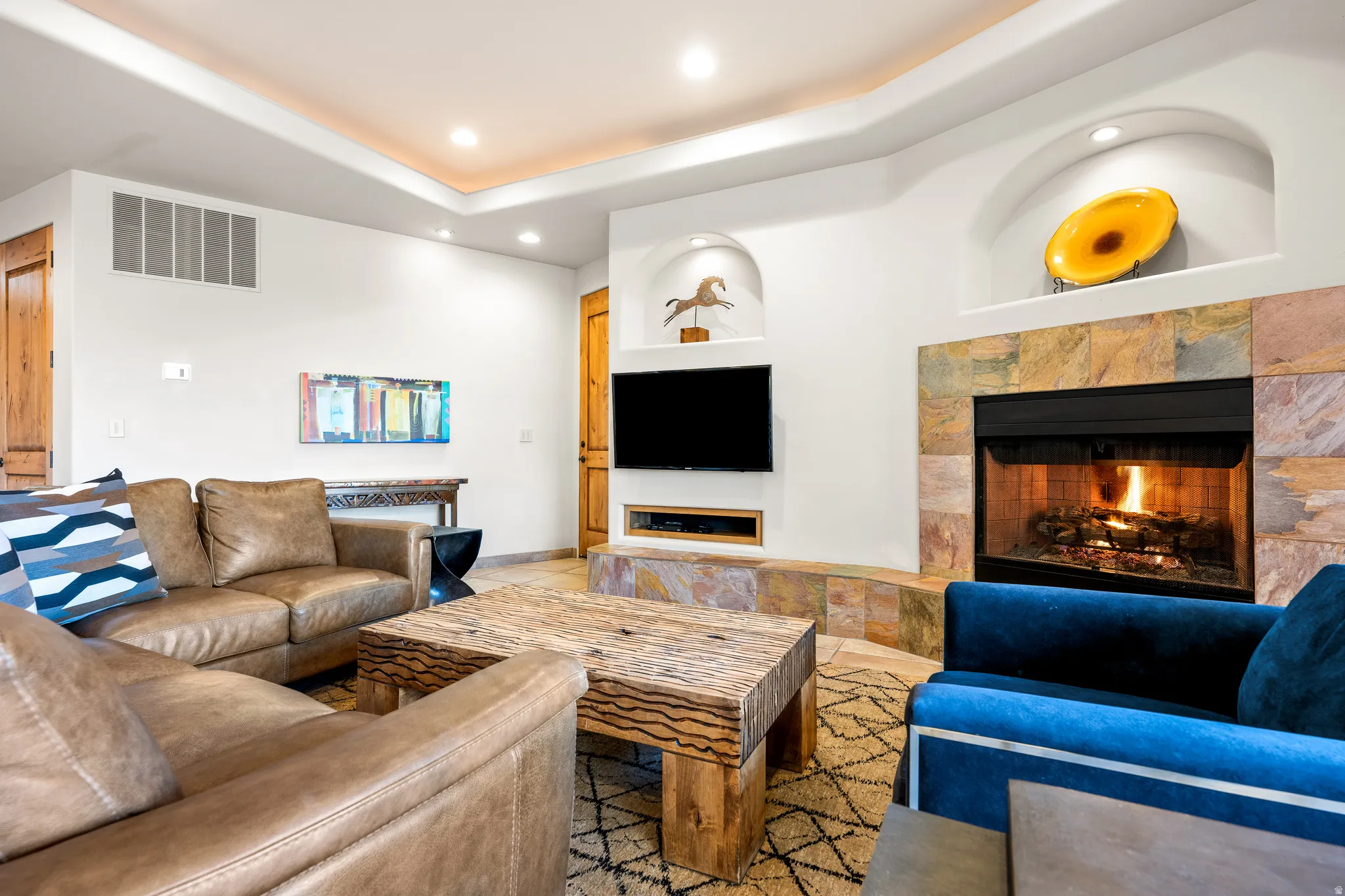 Stacked stone fireplace with integrated media niche, recessed lighting, coved ceiling, and archway niches