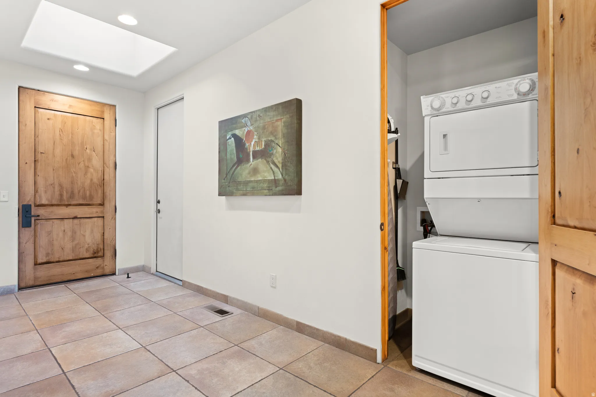 Skylight, recessed lighting, wood-paneled door, tiled flooring, built-in stacked washer and dryer