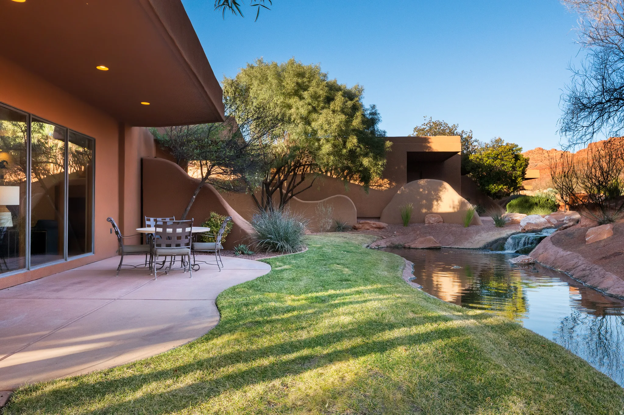 Expansive patio with direct access to a manicured lawn, water feature with waterfall, and natural rock landscaping
