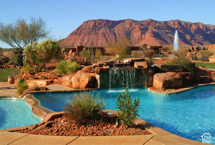 Multi-tiered pool with rock waterfall feature, surrounding desert landscaping, and a distant mountain backdrop