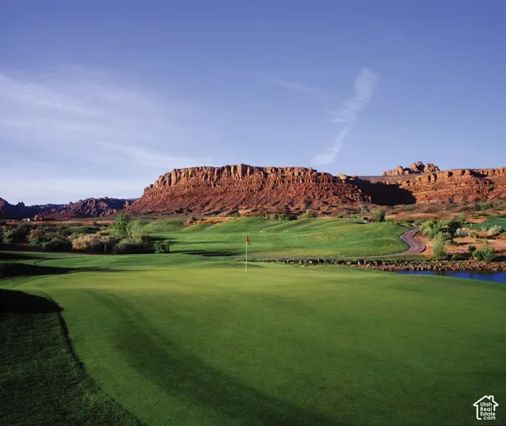 Expansive green with a red flag, surrounded by sculpted fairways and a paved path