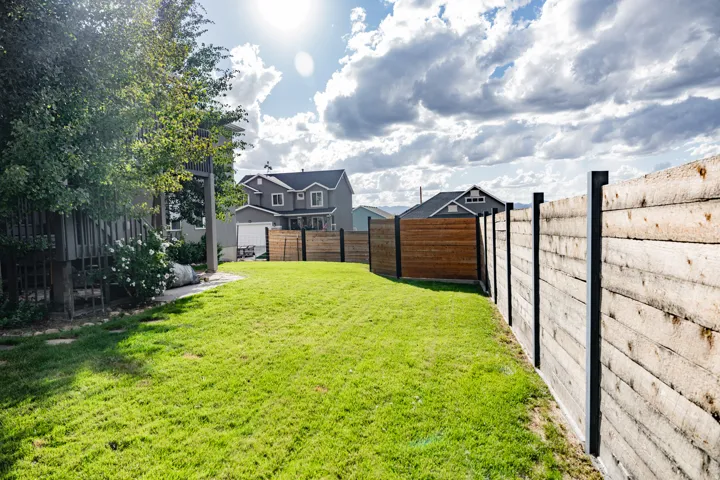 Expansive lawn with a wood plank fence featuring dark posts, a secondary wood fence, and mature trees