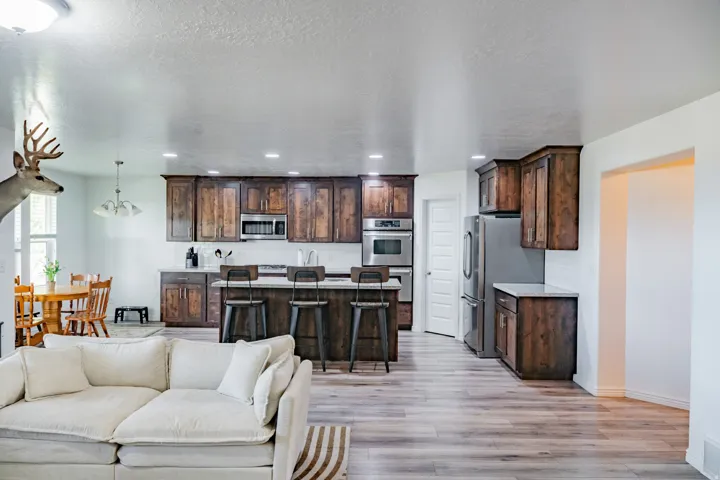 Open-concept living area featuring wood-finish flooring, recessed lighting, and a kitchen with dark wood cabinetry, stainless steel appliances, and light-toned countertops