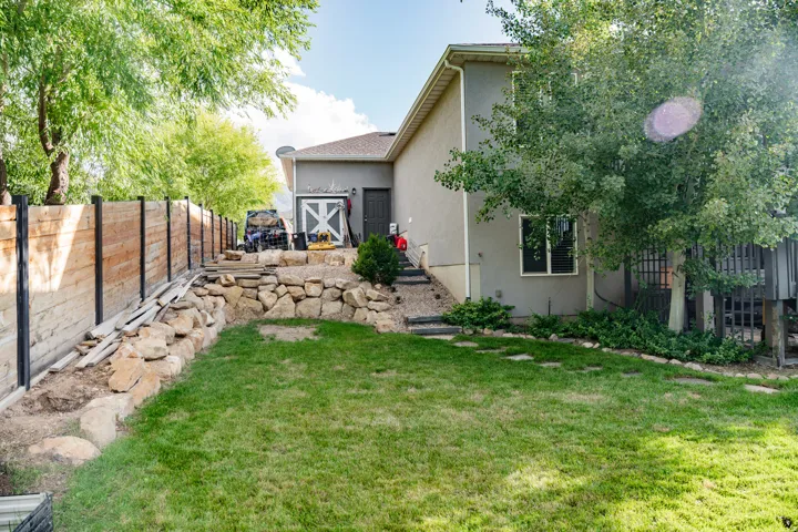 Expansive lawn area with stone retaining walls, mature trees, a wooden privacy fence, and a stucco exterior