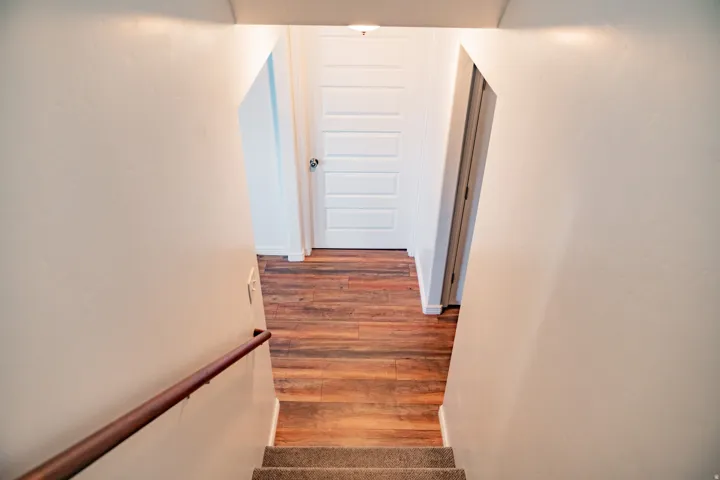 Carpeted staircase with a wood handrail leading to a landing with wood-finish flooring and a paneled door