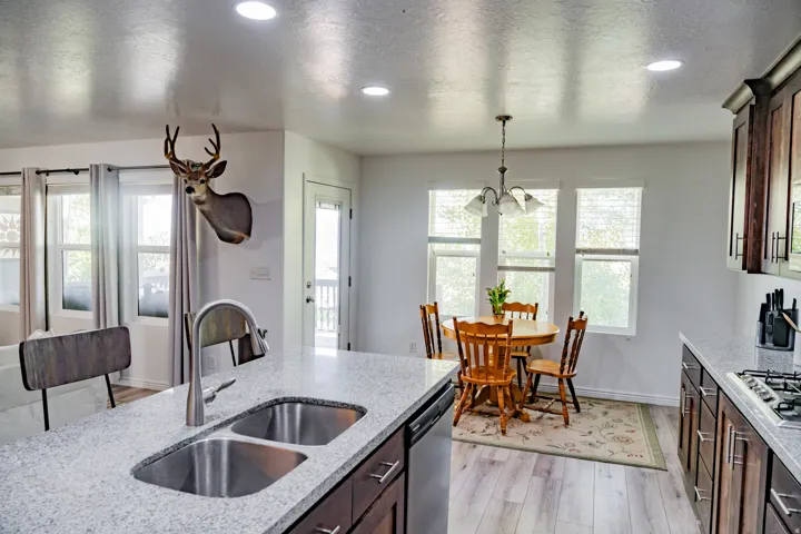 Kitchen featuring an island with double stainless steel sinks, dark wood-finish cabinetry, light-toned countertops, and recessed lighting