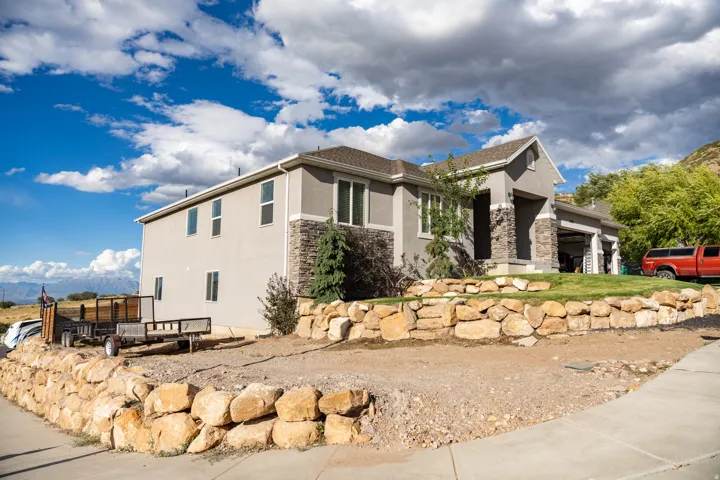 Contemporary architecture featuring a stucco exterior with stone accents, a multi-car garage, and a tiered rock retaining wall
