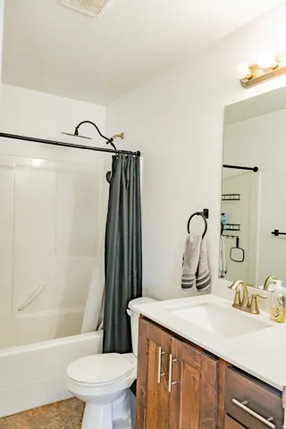 Bathroom featuring a white tub, shower with a rain showerhead, single vanity with wood-finish cabinetry, and a white countertop with an integrated sink