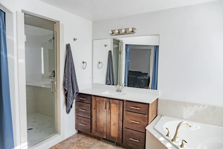 Wood-finish vanity with an integrated sink and light-toned countertop, glass-enclosed shower, and built-in bathtub with a deck-mounted faucet