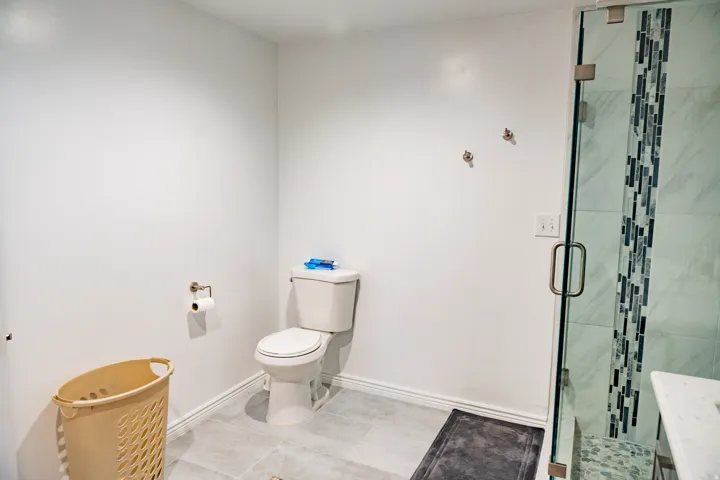 Glass-enclosed shower with a mosaic tile accent strip and light-toned wall tiles, complemented by light-toned floor tiles