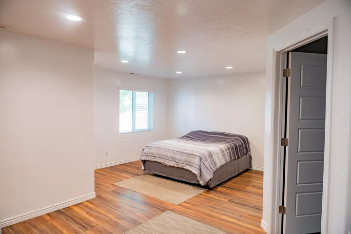 Recessed ceiling lighting, wood-finish flooring, white walls, window with blinds, and paneled interior door