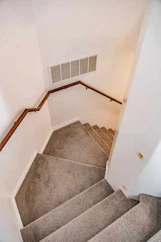 Carpeted stairs with a corner landing and wood handrail