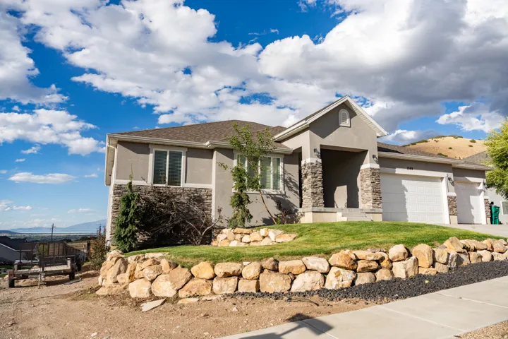 Stucco and stone exterior, covered entry, attached multi-car garage, and a stacked stone retaining wall