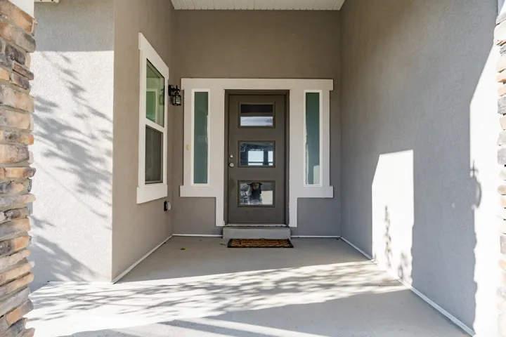 Covered entry featuring a modern dark gray door, flanking vertical windows, an overhead light fixture, and stone accent pillars