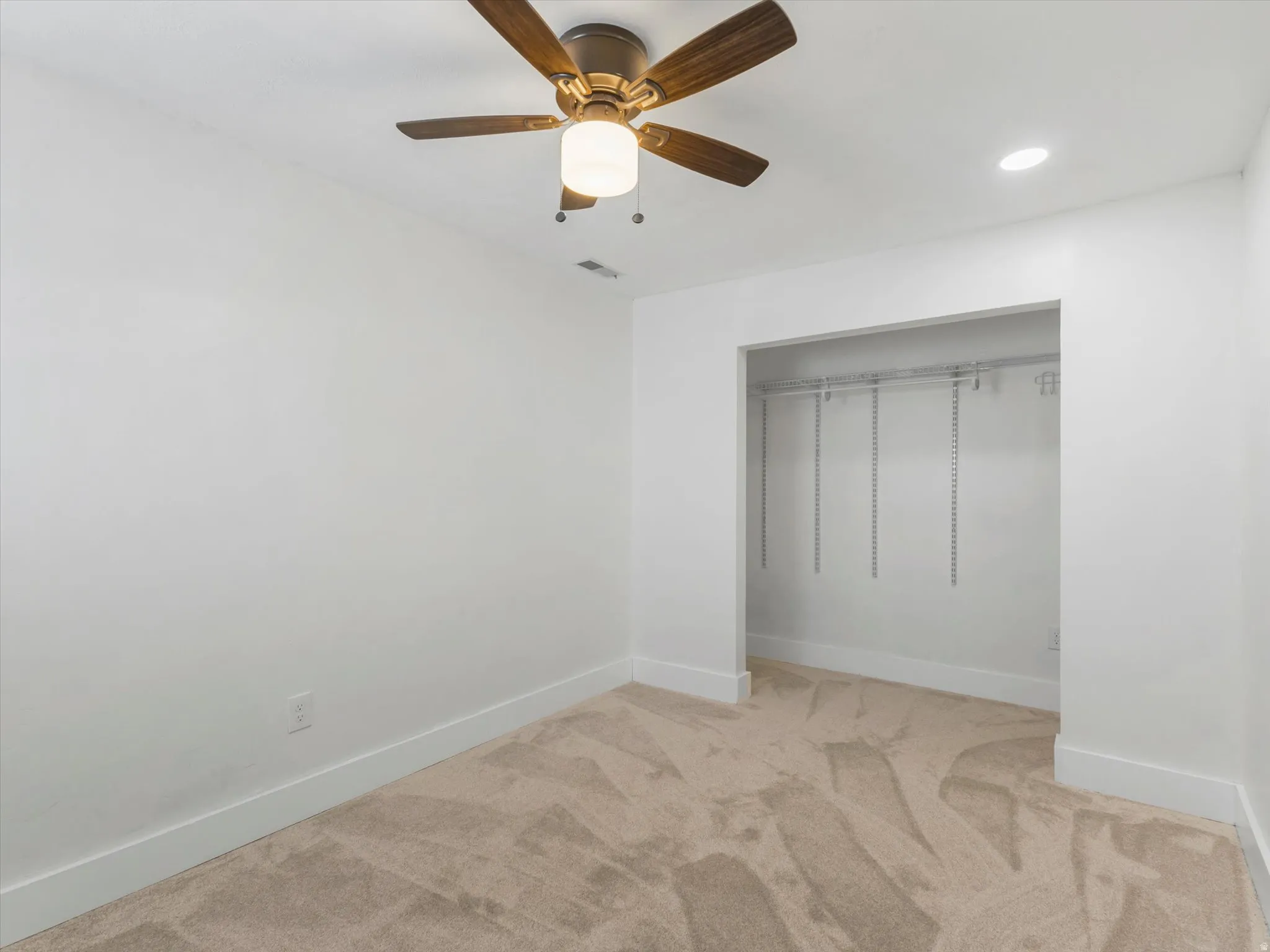 Recessed lighting, ceiling fan with light fixture, light-toned carpeting, and an open closet with wire shelving