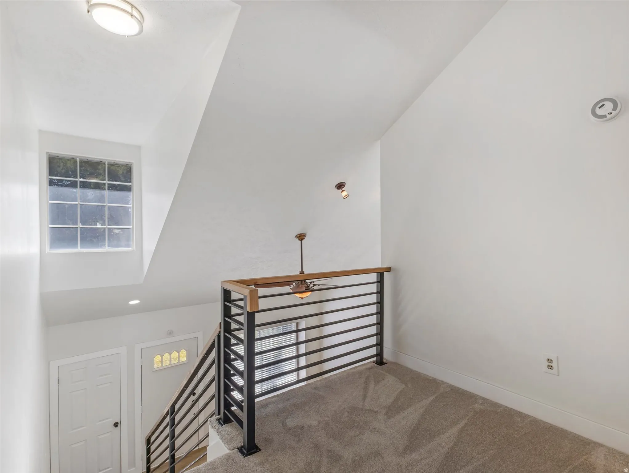 Interior loft space right outside of Master Suite, with vaulted ceiling, carpet flooring, and a modern horizontal bar railing with wood-finish top rail