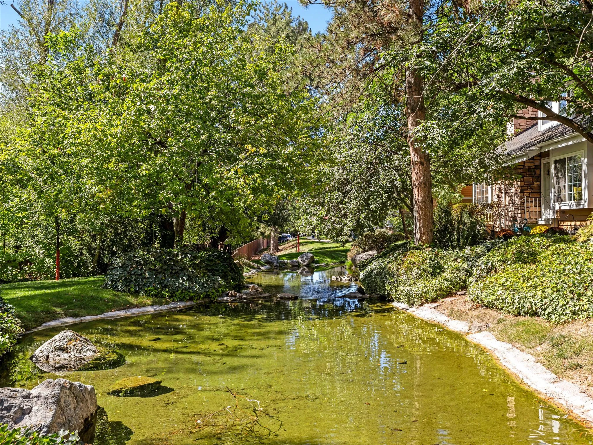 Manicured landscaping, mature trees, and a tranquil water feature with natural rock elements