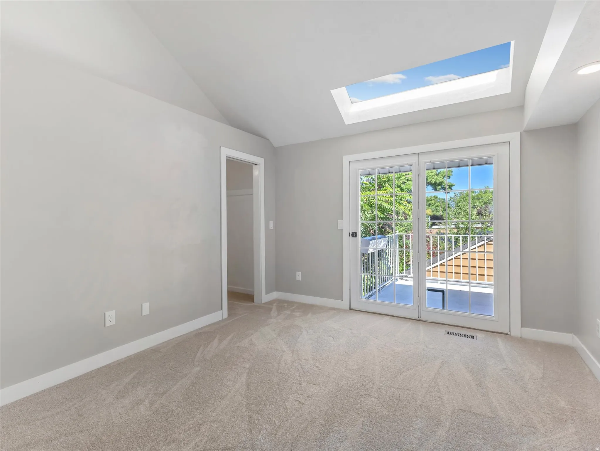 Master bedroom with French doors leading to an exterior balcony, skylight, vaulted ceiling, and neutral carpet flooring
