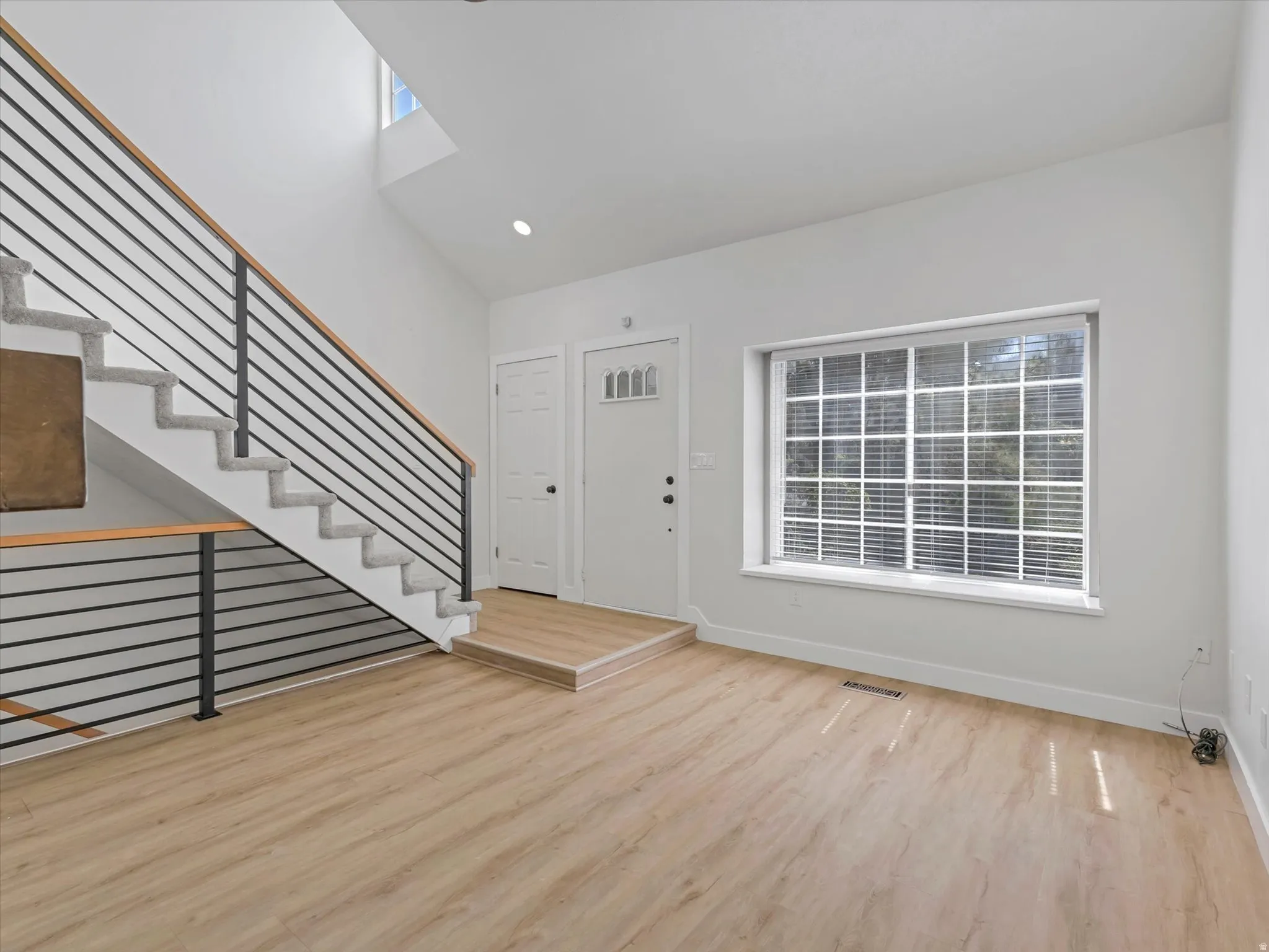 High ceilings with skylight, modern metal and wood railing, wood-finish flooring, recessed lighting, and a large multi-pane window