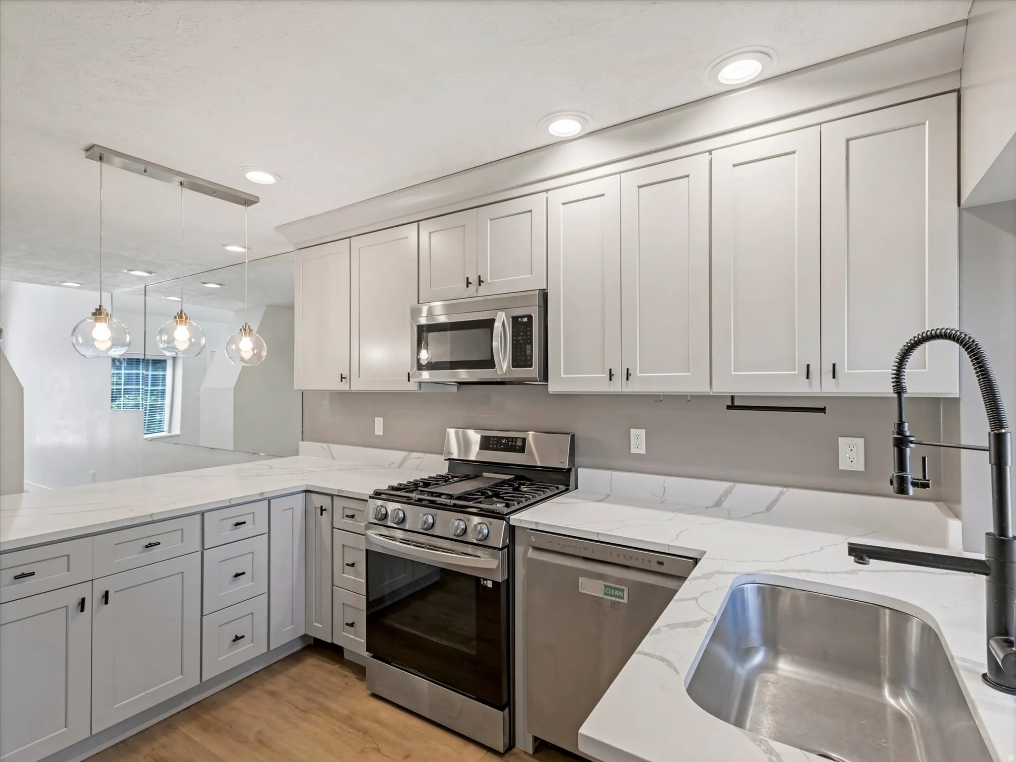 Bright kitchen featuring white shaker cabinetry, stainless steel appliances, white countertops with veining, a stainless steel sink, and wood-finish flooring