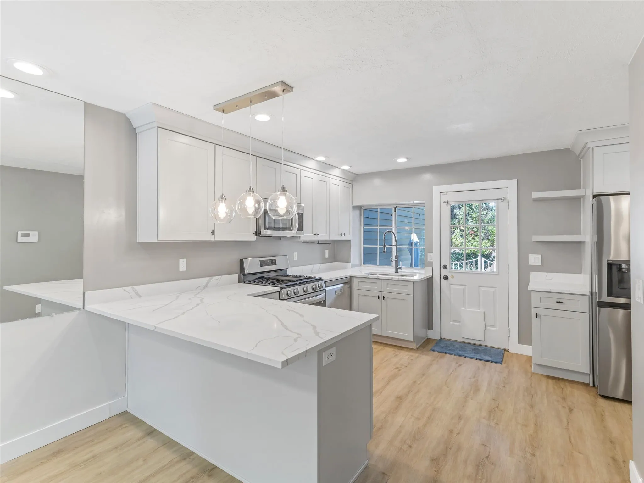 Updated kitchen featuring stone-finish countertops, stainless steel appliances, white cabinetry, wood-finish flooring, and recessed lighting