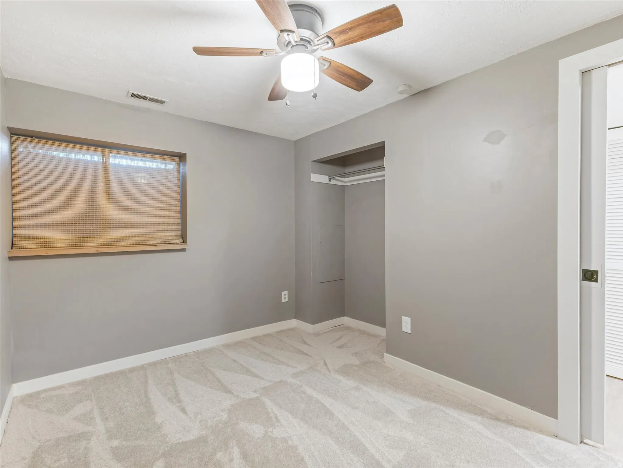 Wall-to-wall carpeting with a light pattern, wood-finish ceiling fan with integrated lighting, and a window with blinds