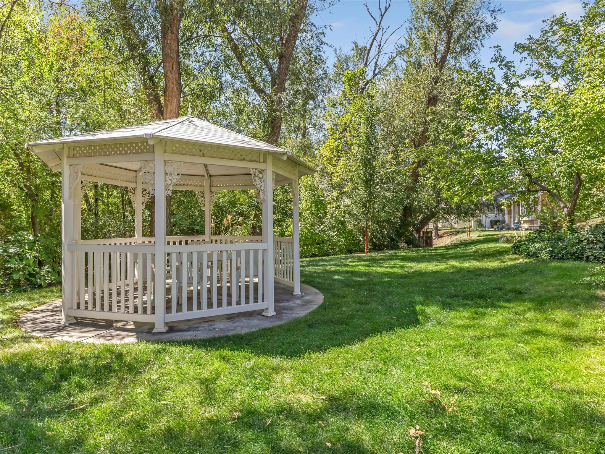 White gazebo with decorative accents, set on a concrete base with a level lawn surrounding it