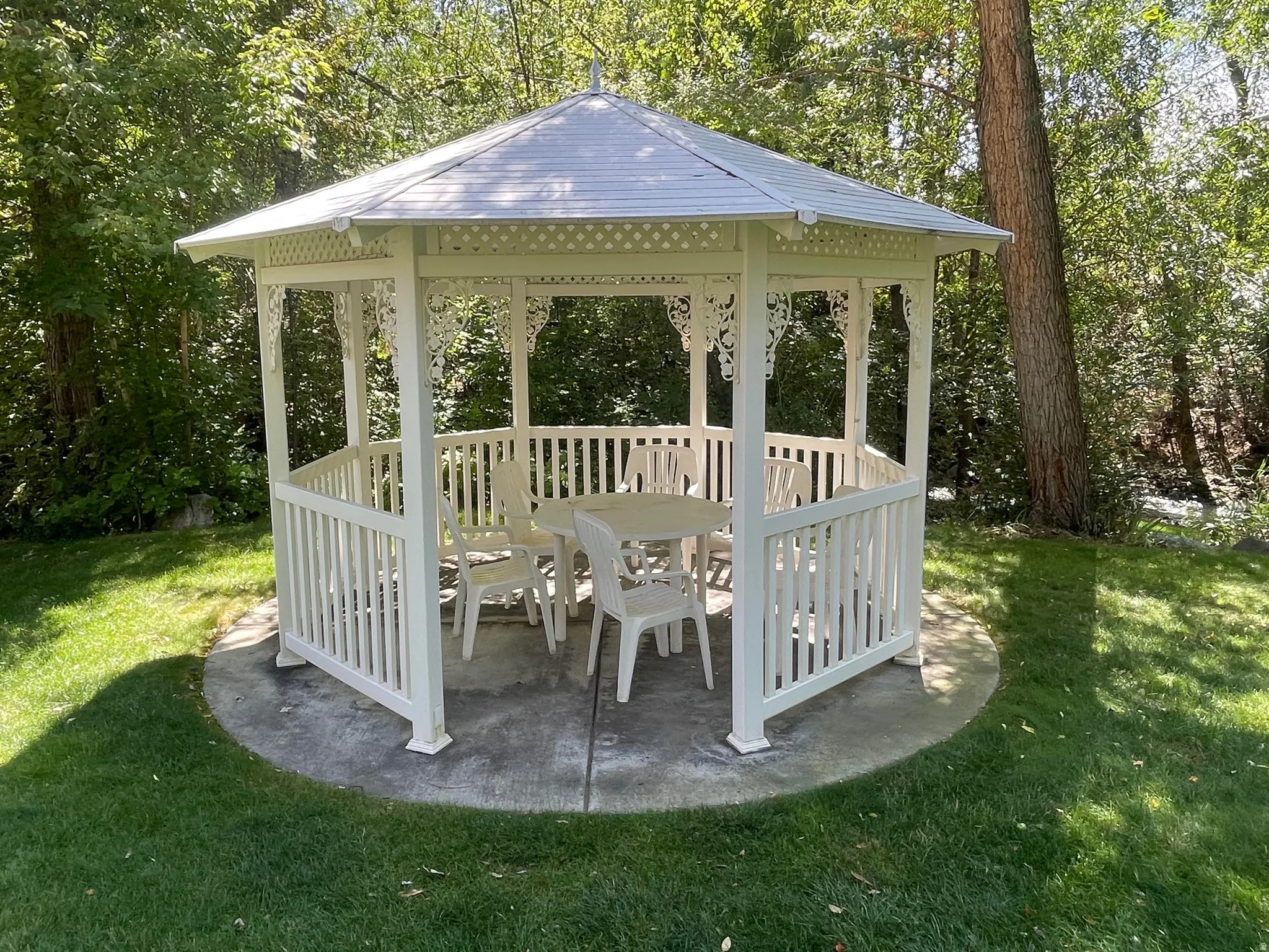 White gazebo with decorative accents, concrete pad, and surrounding lawn