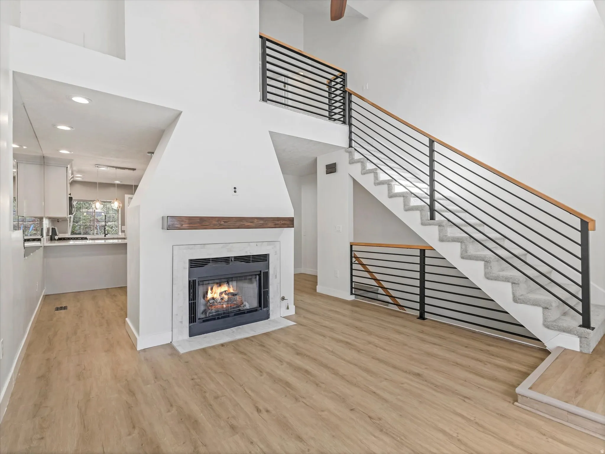 Vaulted ceiling, wood-finish flooring, central fireplace with wood mantel, modern railing staircase, and recessed lighting