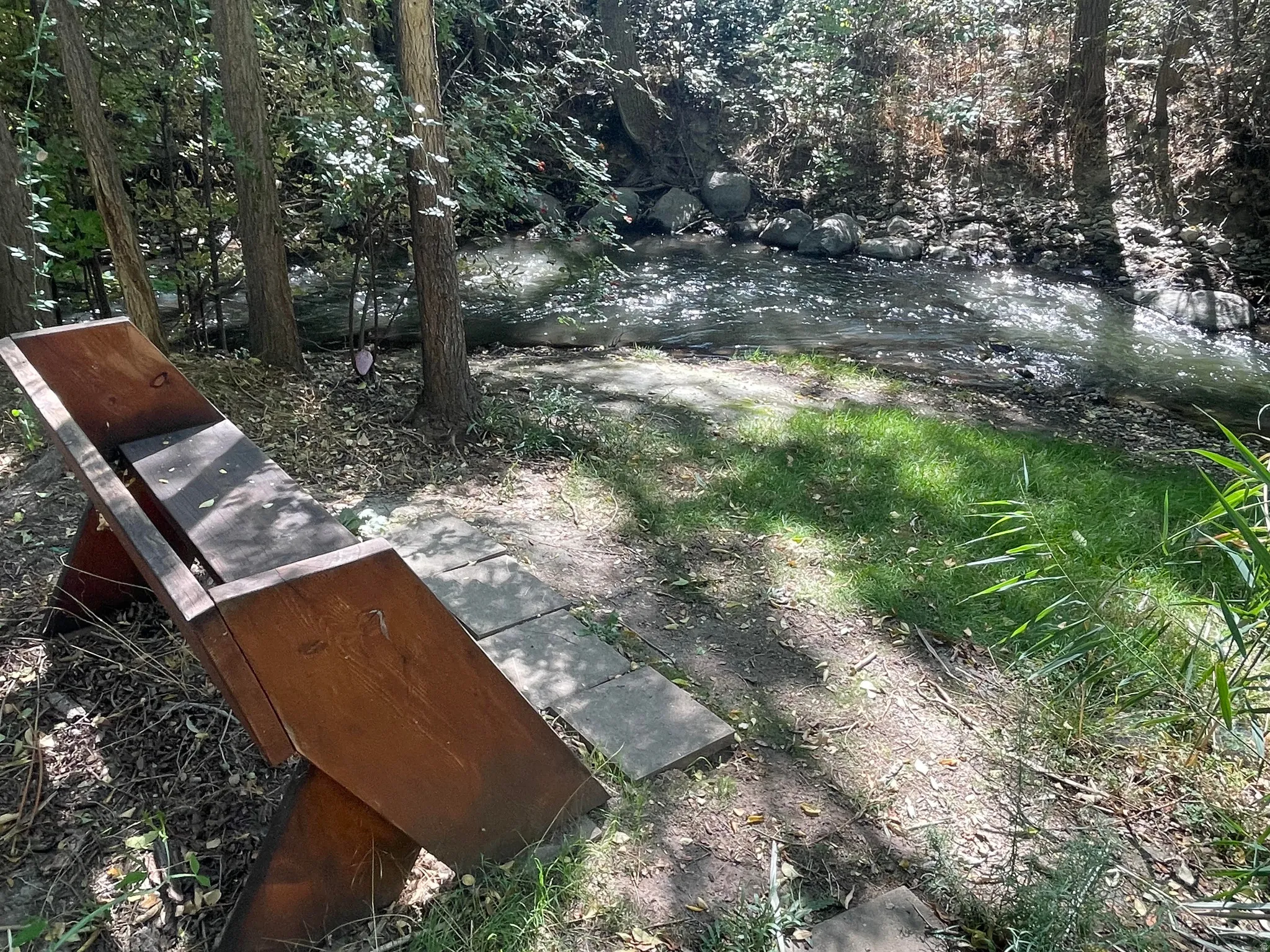 Water feature with natural rock bed, surrounded by mature trees, ground cover, and a wooden bench