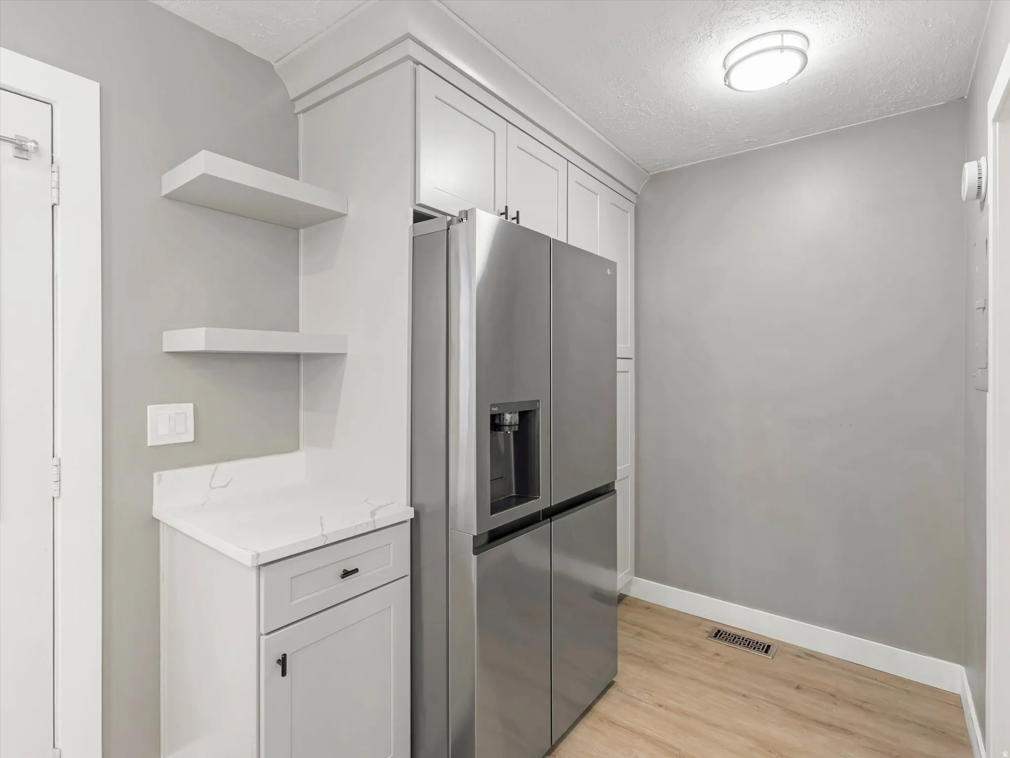 Built-in cabinetry with crown molding, stainless steel refrigerator, floating shelves, light wood-finish flooring, and a flush mount ceiling light