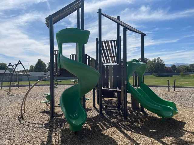 Neighboring Scott Avenue Park - Recreational playground featuring two green slides, climbing elements, and a swing set on a wood chip surface