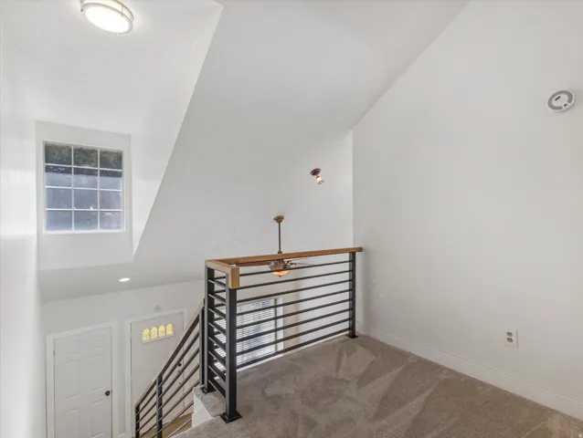 Interior loft space right outside of Master Suite, with vaulted ceiling, carpet flooring, and a modern horizontal bar railing with wood-finish top rail