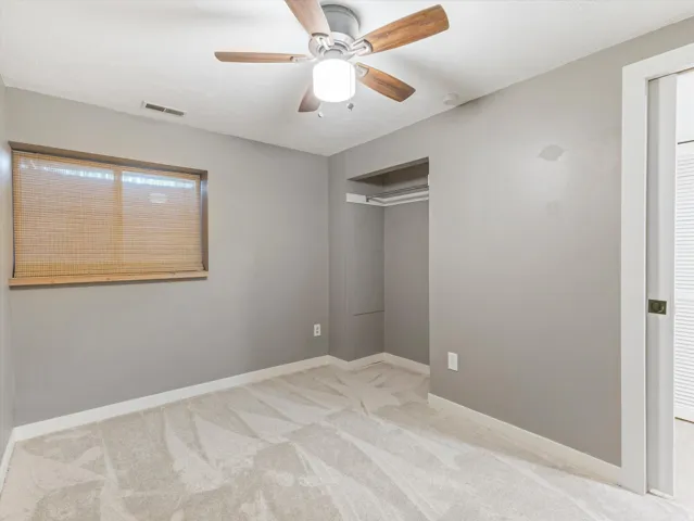 Wall-to-wall carpeting with a light pattern, wood-finish ceiling fan with integrated lighting, and a window with blinds