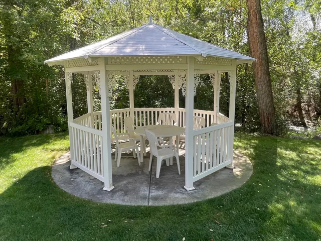 White gazebo with decorative accents, concrete pad, and surrounding lawn