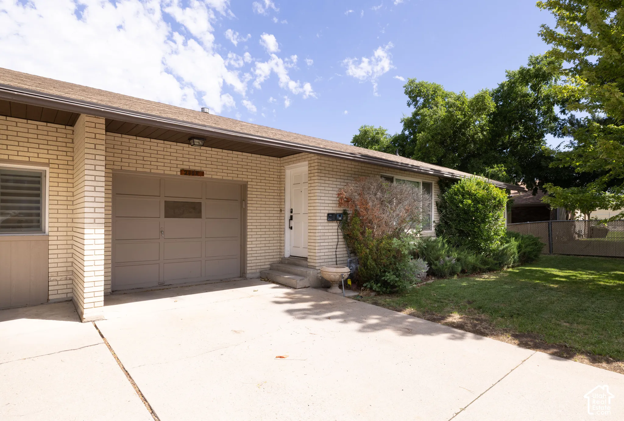 Brick exterior, attached garage, concrete driveway, mature landscaping, and a front entry
