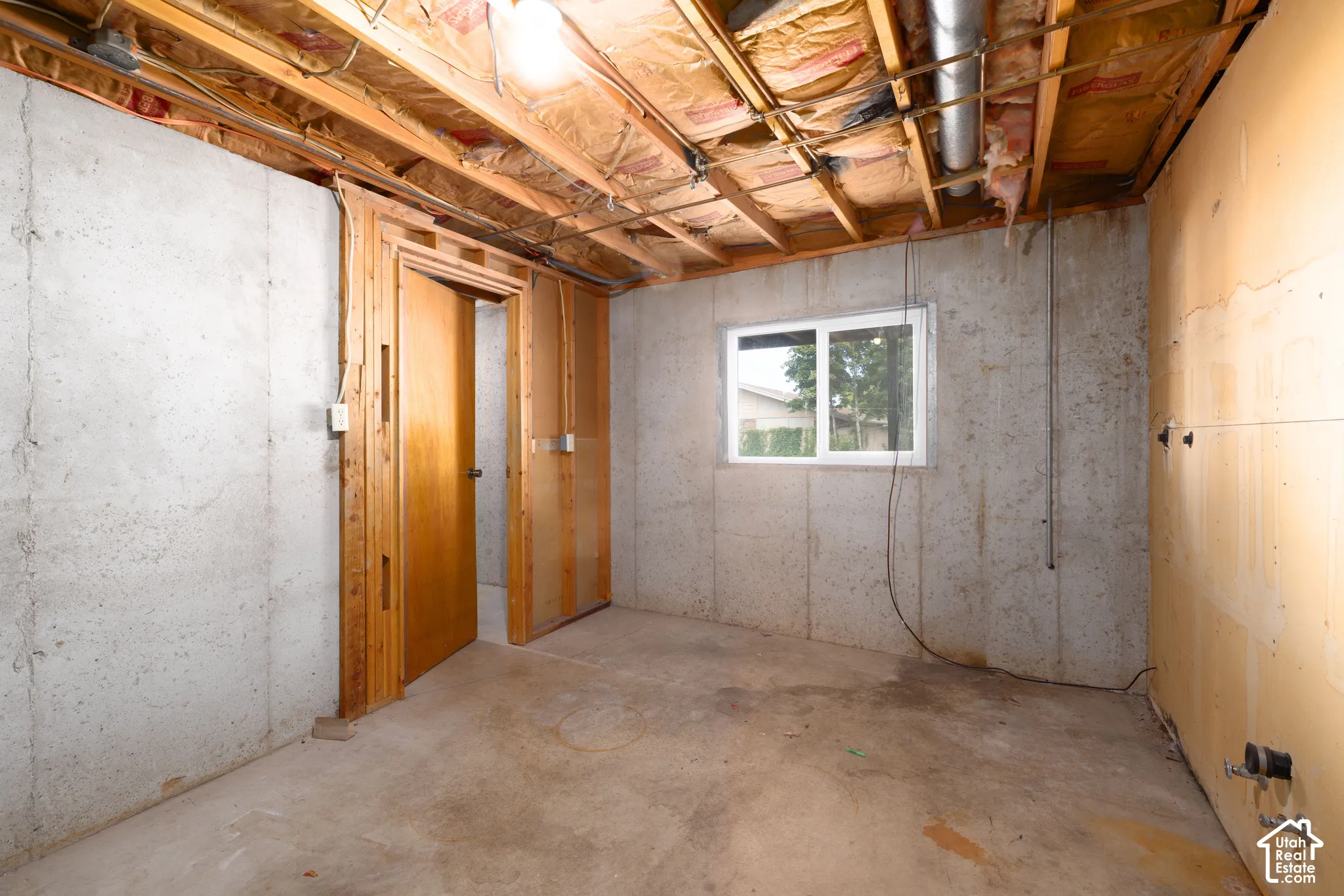Unfinished basement featuring concrete walls and flooring, exposed ceiling joists, and a casement window