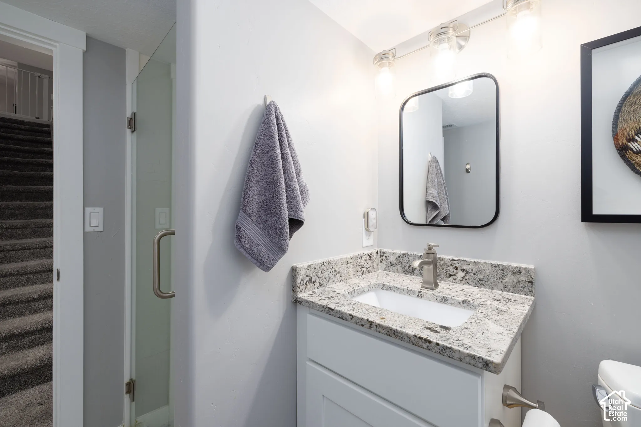 White vanity with a granite countertop, integrated sink, and brushed nickel faucet
