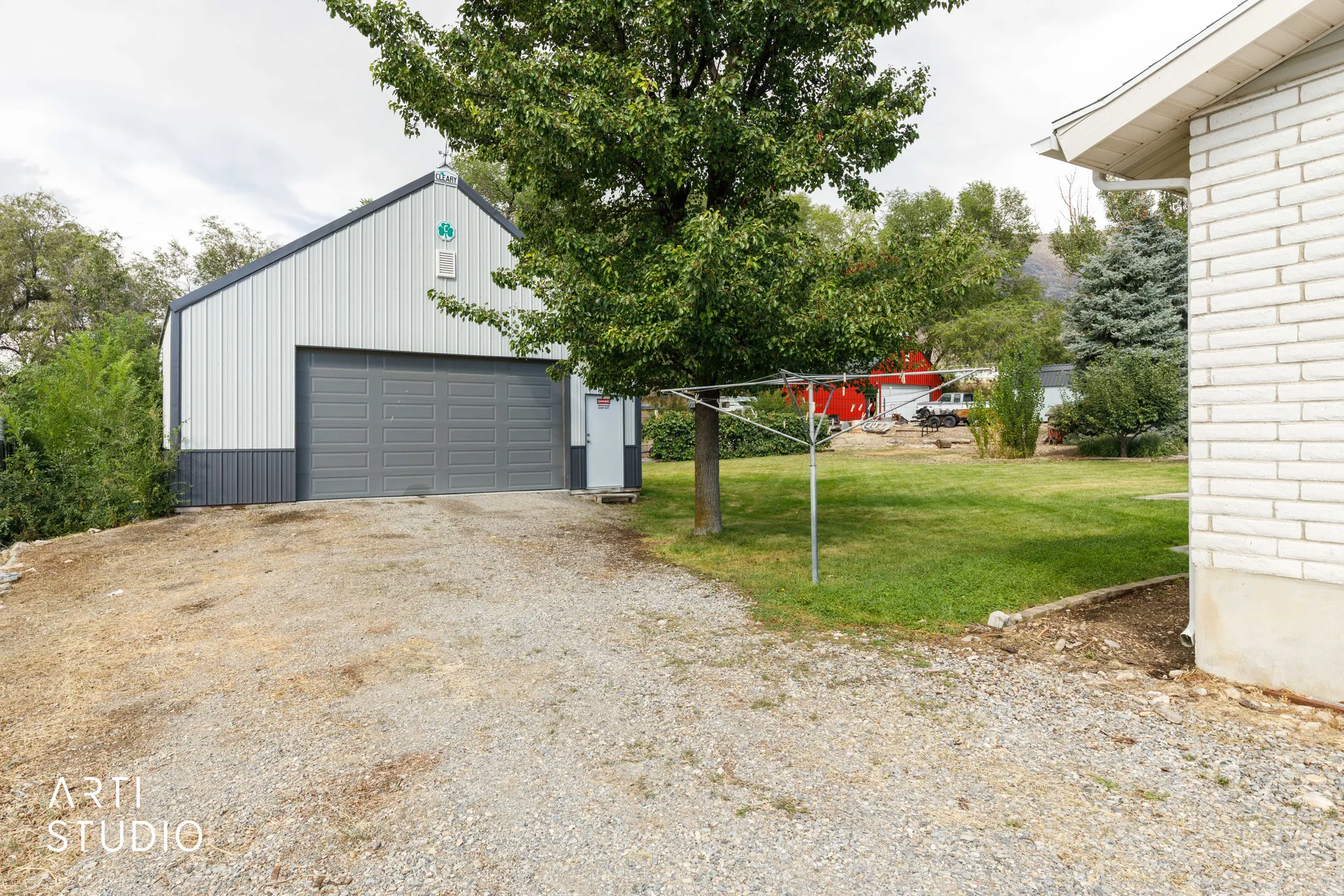 Detached 30 x 30 foot metal-sided shop with a large gray overhead door, gravel driveway, and a white brick-sided structure