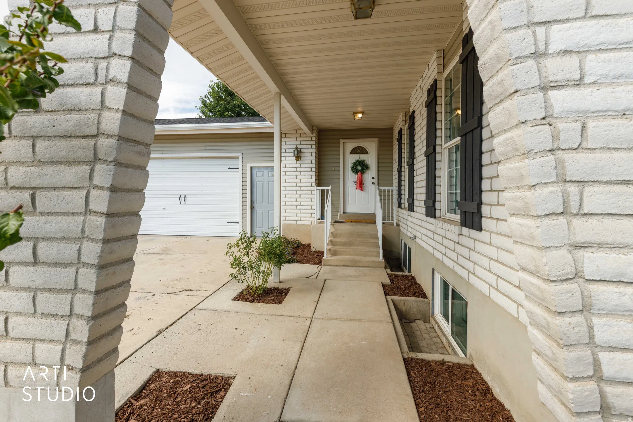 White brick exterior with black shutters, covered entry porch, concrete walkway, and a two-car garage